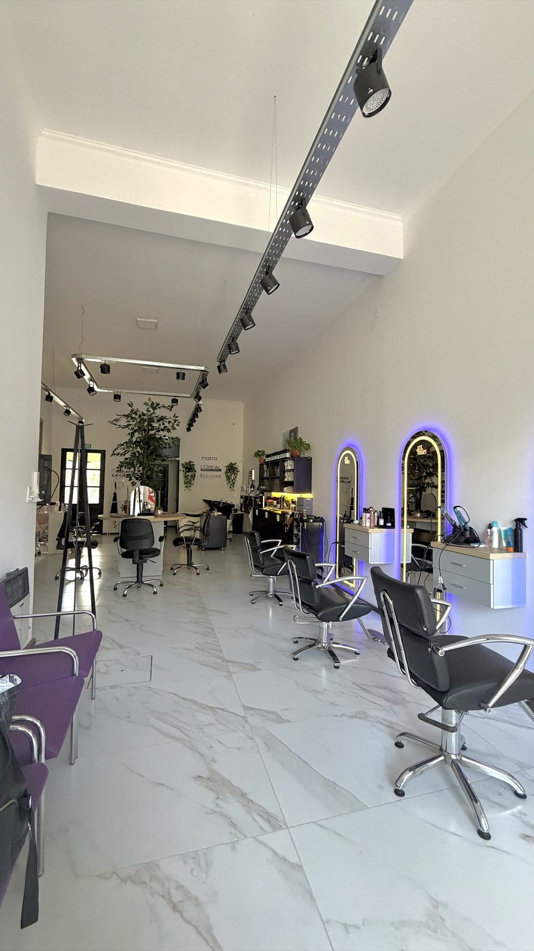 Interior del salón Just Dollies con piso de mármol, sillones negros y espejos en arco